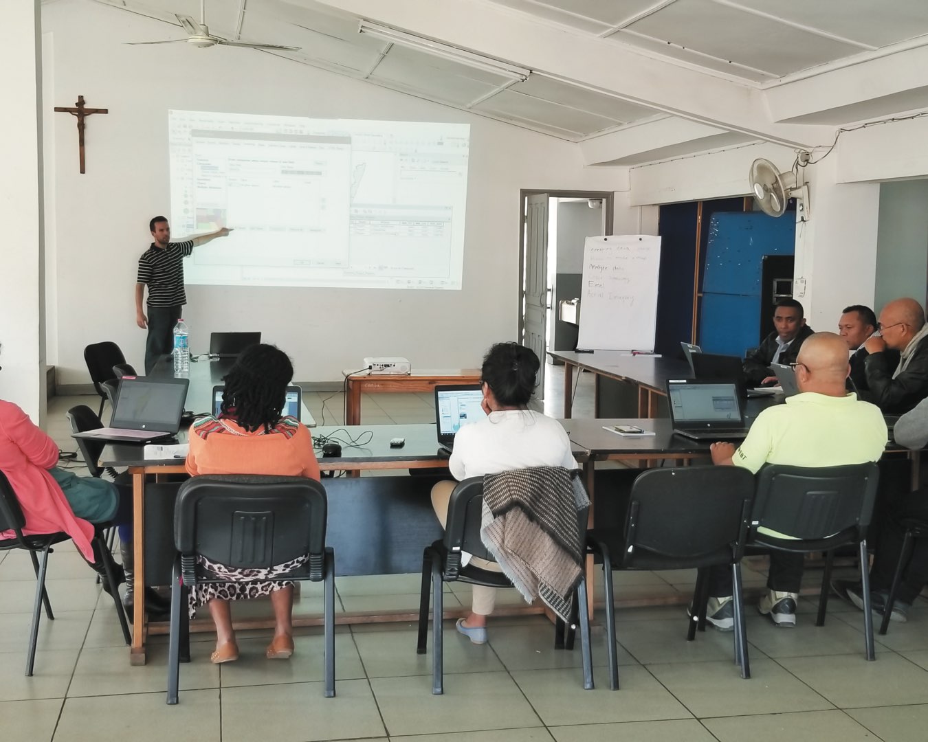 Eric Wagner stands at the front of a Malagasy classroom presenting to a group of eight CRS partners sitting around the table