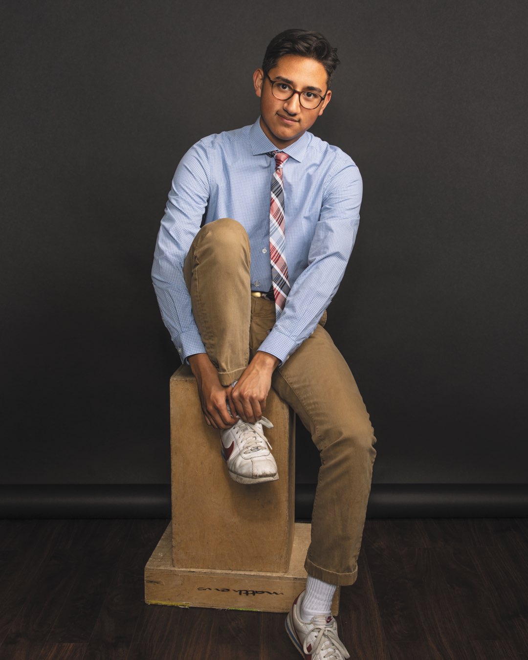 Rising senior Anthony Freay tying his sneaker in tan khakis, a blue dress shirt and patterned tie