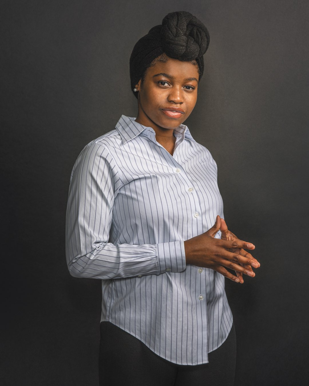 Sheydline Moise wearing a black headwrap in a pinstripe blouse and black slacks