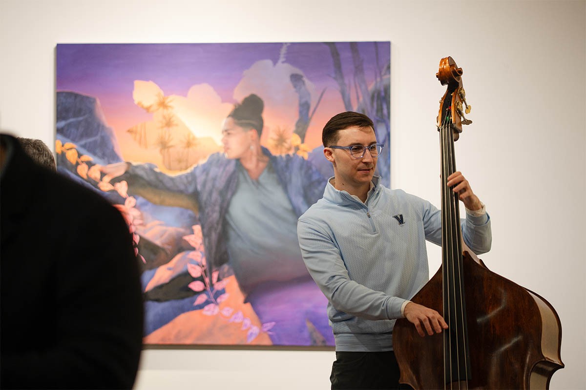student-involvement-art-gallery Individual playing the chello at an art exhibit with a painting in the background