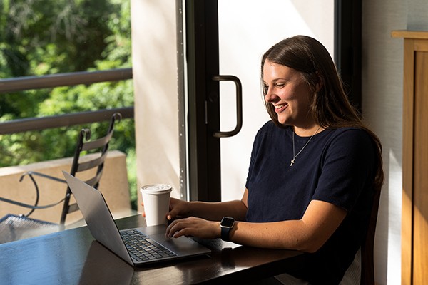 igrad-financial-page student sitting in windowsill looking at laptop