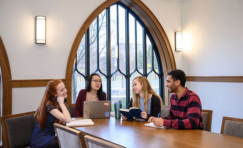 Students sit around a table in a discussion Students sit around a table in a discussion