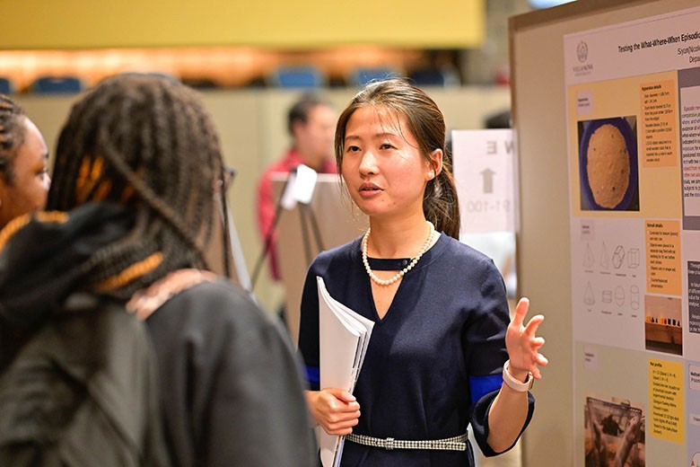 crop-female-talk-sympos Woman speaking to student holding papers.