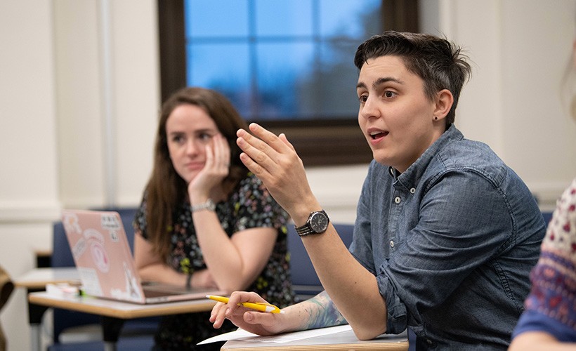 Student speaks in a classroom A student speaks in a classroom with another student in the background.