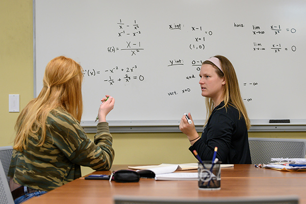 Students work together, writing equations on a whiteboard.