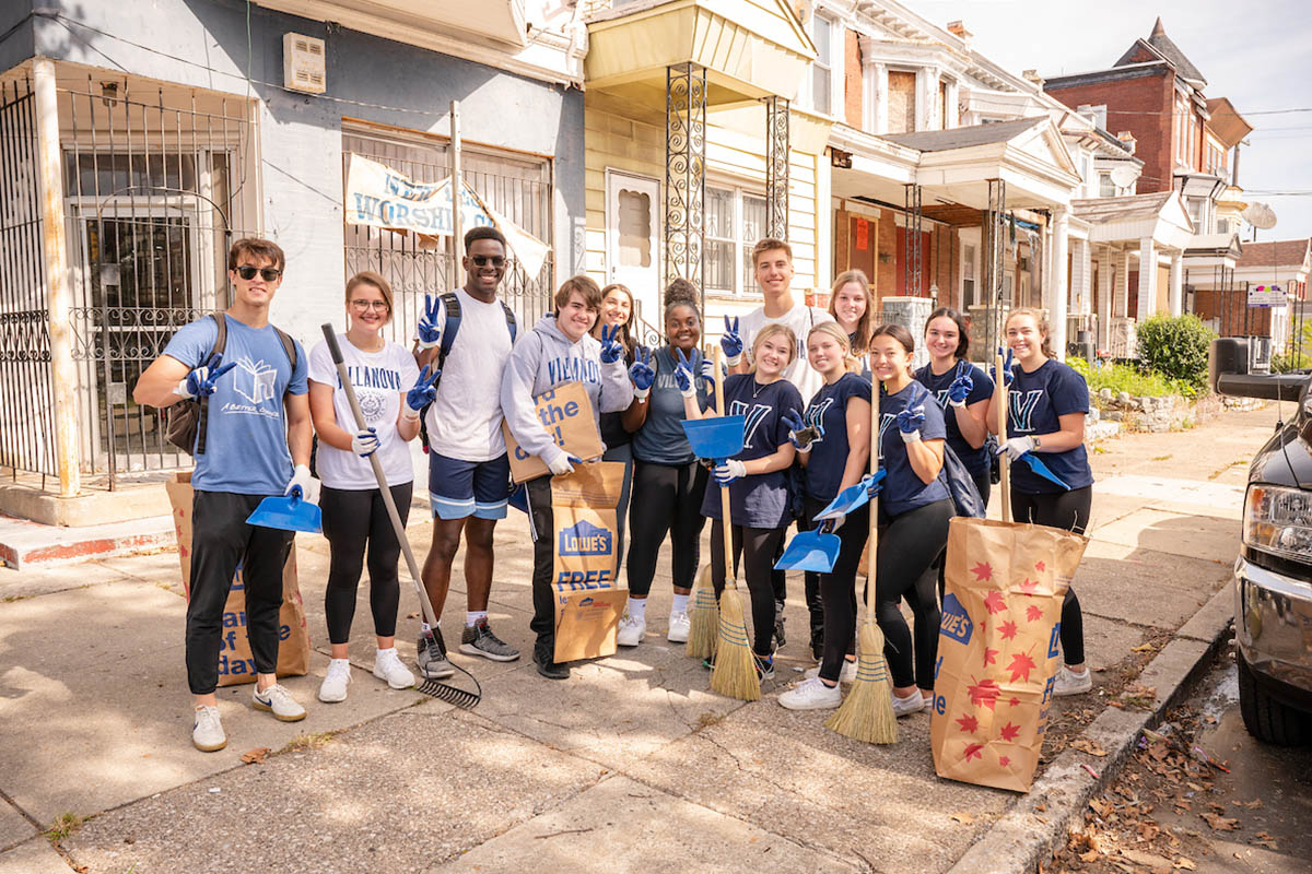 Students doing service, throwing up the Villanova V with rakes and bags