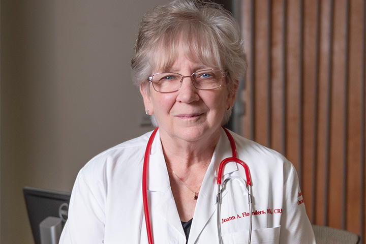 Jo Ann Flounders wearing a red stethoscope around her neckand white lab coat with her name on it.