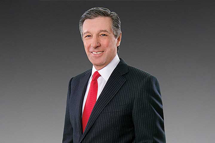 Daniel DiLella wearing a dark business suit and a red tie.